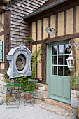 Rustic house façade with light green wooden door and small, green garden seating area