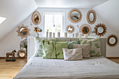 Bedroom with sloping ceiling, white and green bed linen and rattan mirrors on the wall