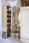 Vintage shelf with porcelain crockery and antique clocks next to an old cupboard and chair