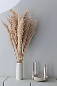 Bouquet of dried pampas grass flowers in a white vase next to a ceramic bowl with stick candles