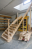 Wooden staircase under construction in a carpentry workshop with accessories and tool shelves