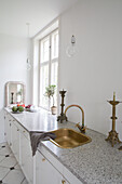 Kitchen with white cupboards, brass sink and candlesticks