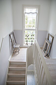 Light-colored wooden staircase with white walls and window, empty picture frame on the landing