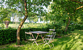 Holztisch und Stühle unter Bäumen im Garten