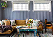 Living room with wood panelling, mustard yellow sofa and wooden table in a shabby chic look