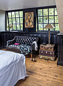 Bedroom with leather sofa and antique suitcases in front of mullioned windows