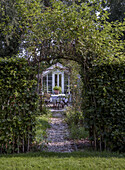 Garden path with gravel and arbour arch leads to a greenhouse with seating area