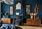 Fireplace and chests of drawers in bedroom with dark blue wall and herringbone parquet flooring