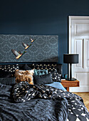 Bedroom with dark blue wall, patterned bed linen and black bedside lamp