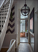 Hallway with geometric wall tiles and globe light, view into the bathroom with free-standing copper bathtub