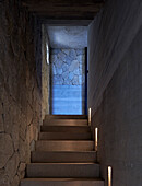 View from bottom of an illuminated concrete staircase between stone and concrete walls