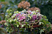 Herbstarrangement aus Hortensien (Hydrangea) und Beeren, Hopfenranken (Humulus) auf rostigem Gartentisch