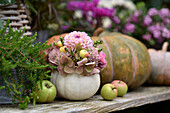 Herbstliches Arrangement mit Zierkürbisvase, Hortensienblüten, Dahlien (Dahlia), Zieräpfel und Äpfel auf Holztisch