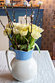 Gelbe Tulpen (Tulipa) und Kirschzweige in blau-weißer Kanne