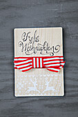 Wooden sign with Merry Christmas" lettering and red and white bow"