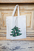 Stofftasche mit Weihnachtsbaum-Motiv vor Holzwand