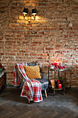 Vintage armchair with chequered woollen blanket and side table on castors in front of brick wall