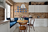 Küche mit Essbereich, blauer Eckbank, Ziegelwand und Deko-Tellern an der Wand