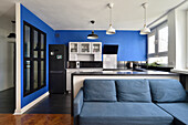 White and black kitchen with blue wall, dark floor open to living area