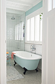 Freestanding bathtub with metal feet in front of window with louvre blinds in bright bathroom