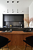 Modern kitchen with black cabinets, wooden table and pendant lights