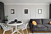 Room with white dining table and dark grey sofa, pictures on the wall