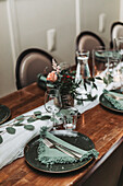 Gedeckter Esstisch mit dunkelgrünen Tellern und Blumendekoration