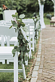 Weiße Stühle dekoriert mit Eukalyptuszweigen für eine Outdoor-Feier