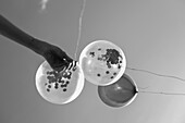 Hand holding balloons filled with confetti, black and white photography