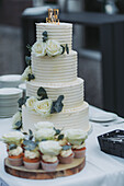 Hochzeitstorte mit Rosendekor und Cupcakes auf Holzbrett