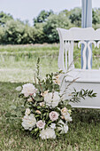 Blumenarrangement mit Pfingstrosen und Rosen vor weißer Vintage-Bank im Sommer