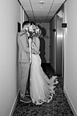 Hochzeitspaar küsst sich im Flur mit Blumenstrauß und eleganter Kleidung