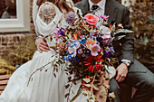 Braut mit ausgefallenem Blumenstrauß und Bräutigam im Anzug bei Hochzeitsfeier