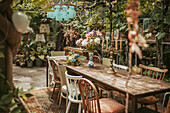 Wooden table with flowers and candles, various wooden chairs in a greenhouse with lots of plants and vintage decorations