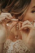 Frau befestigt Ohrring, trägt Brautkleid mit Spitze