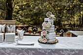 Wedding cake with rose decoration on wooden disc, lace tablecloth, cake plates and cake forks, outdoors