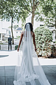 Bride in long white dress and veil approaches groom outdoors