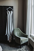 Wedding dress hanging on wardrobe, green velvet armchair next to it