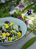 Schüssel mit Wildblumen und Kräutern auf weißem Tuch