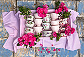 Cups in pink and arranged with flowers on a checkered cloth