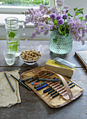 Table with pencil case, pens, peanuts and bouquet of lilacs in glass vase