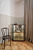 Glass cabinet and wooden chair next to pleated curtain in three-room apartment