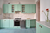 Mint green kitchen with marble worktop and backsplash and gerbera daisies in vase
