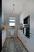 Functionally designed kitchen with white front and patterned floor tiles