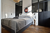 Schlafzimmer mit grauer Tagesdecke, schwarzem Raumteiler und Fischgrätparkett