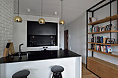 Modern kitchen with golden pendant lights, bar stools and bookshelf