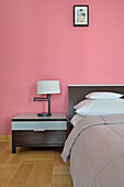 Modernes Schlafzimmer mit pinker Wand und dunkler Nachttischkommode
