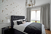 Schlafzimmer mit gepolstertem Bett und floralem Tapetenmuster
