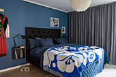 Bedroom with dark blue wall, double bed and patterned blanket