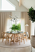 Dining room with round wooden table, designer chairs and modern chandelier